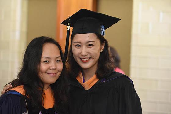 Photo of two young women in graduate caps and gowns, posing for the camera