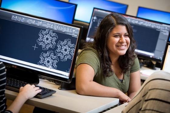 Photo of a Chatham University student sitting between computers in lab smiling. 